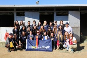 Team photo in front of stables, holding ribbons and flags