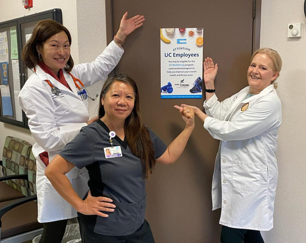 Three women point at a white sign hung on a door.