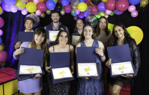 A group of students holds their awards for academic excellence in blue folders.