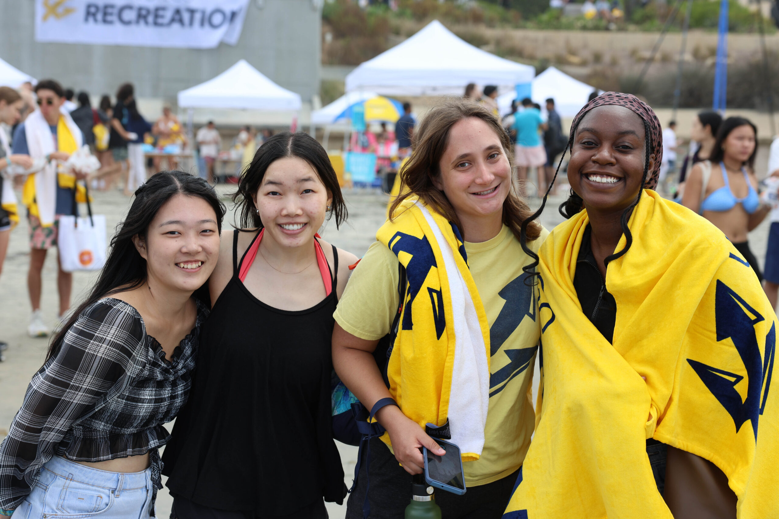 A group of four college-age women stand on a beach, smiling together.