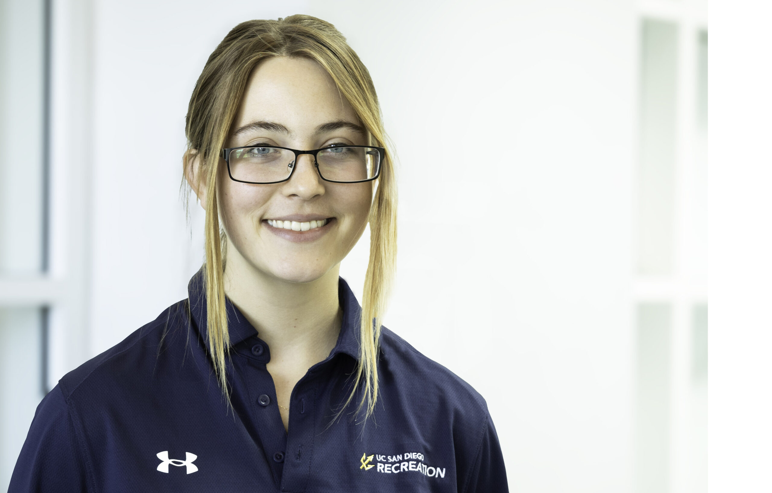 Emma is a white woman with medium-length light-brown hair, wearing a blue polo and glasses.