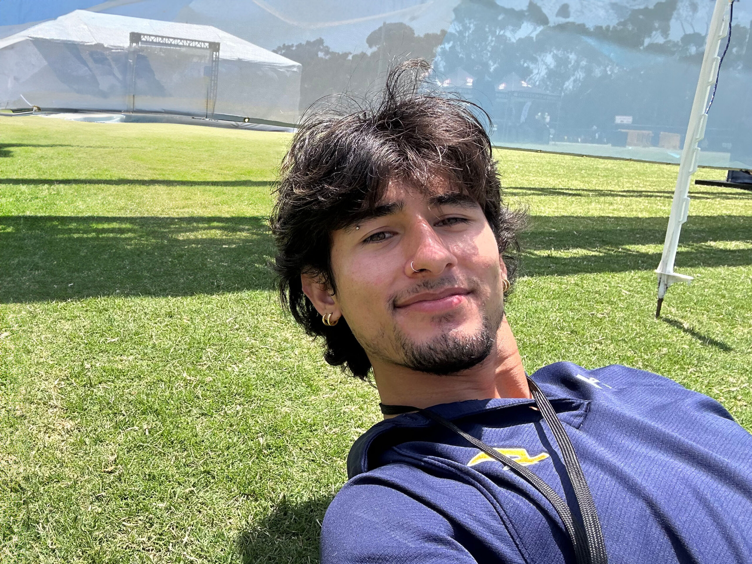 Alex Castaneda, a young man with medium-length brown hair, relaxes by laying in the grass in the sun.