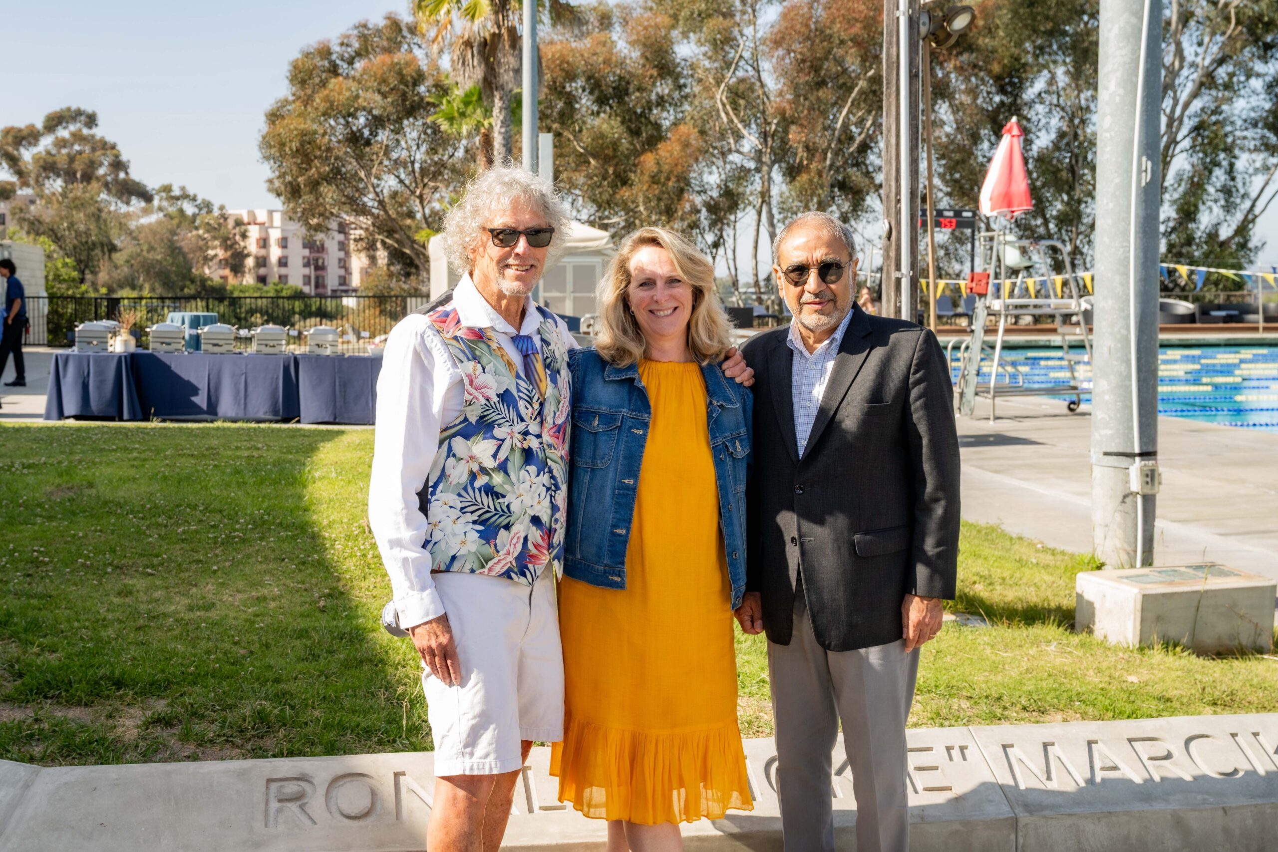 Three people stand shoulder-to-shoulder alongside a pool: Ronald “Sickie” Marcikic, Vice Chancellor of Student Affairs & Campus Life Alysson Satterlund, and Chancellor Pradeep Khosla.
